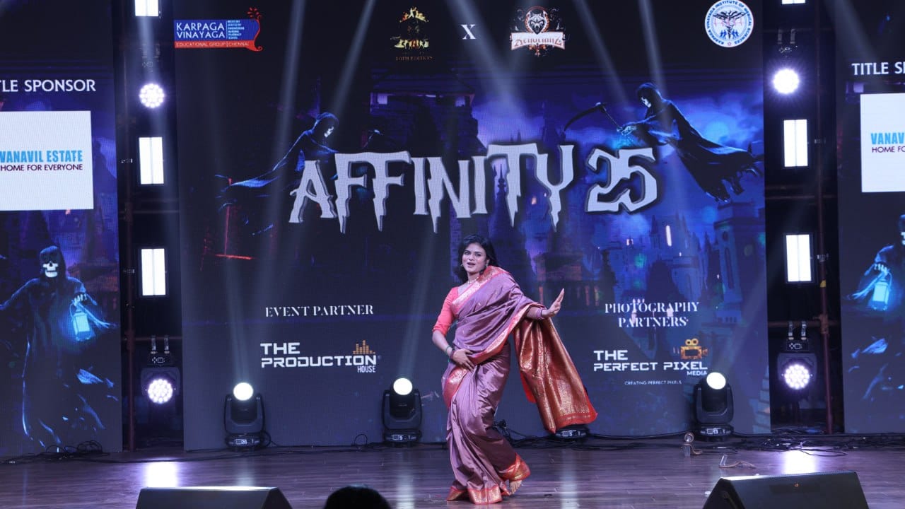 A dancer in a saree performs mid-movement on stage in front of an illuminated AFFINITY backdrop and sponsor boards.