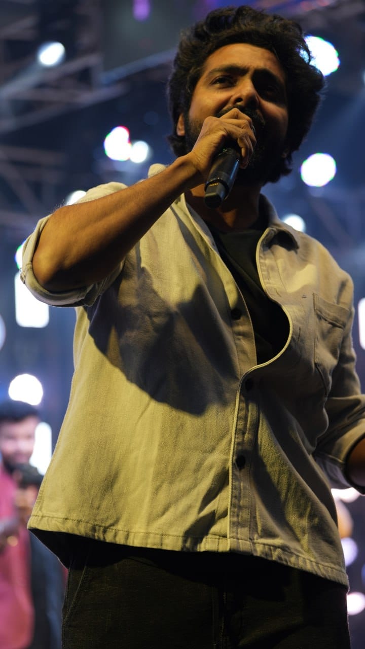 A performer sings into a handheld microphone under stage lighting.